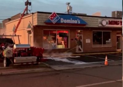 employee pressure washing a concrete walkway and roof of Domino's in Long Branch. NJ