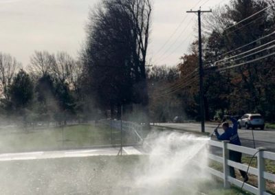 employee power washing a white picket fence in Holmdel, NJ