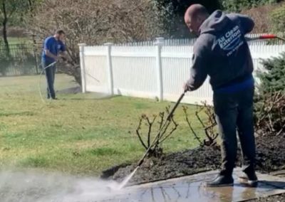 two employees, one power washing a paver walkway while the other power washes a fence in Holmdel, NJ